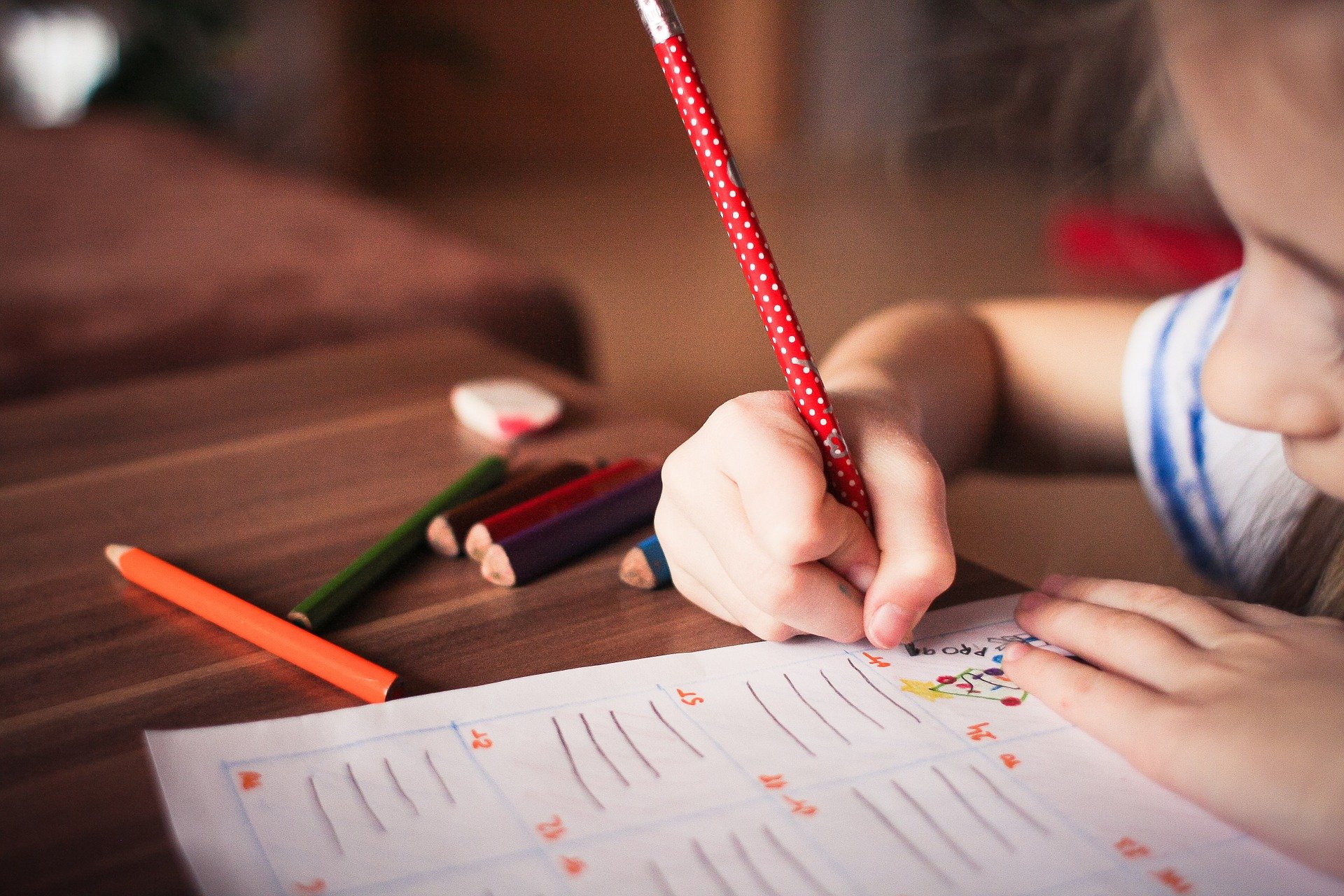 Niña escribiendo en un cuaderno con lápices de colores, simbolizando el proceso educativo en un entorno de aprendizaje creativo.