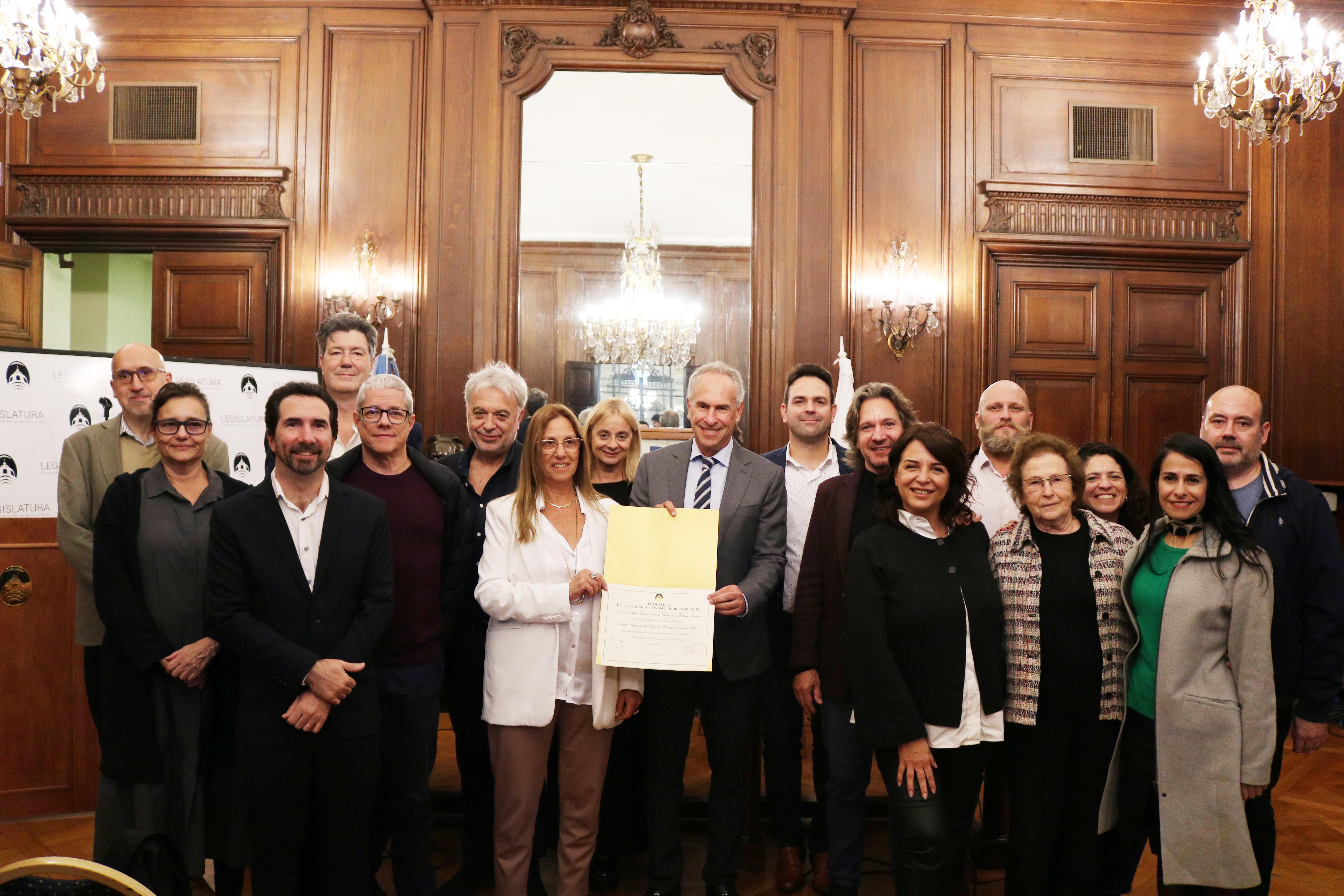 Un grupo de personas en un evento institucional posan con un documento en un salón elegante, representando una ceremonia destacada.