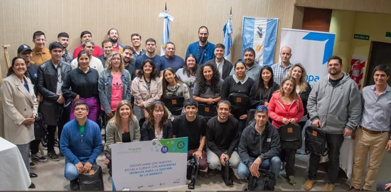 Capacitación docente en energía con grupo de personas sonrientes posando con banderas argentinas y un cartel de certificación en un evento institucional.