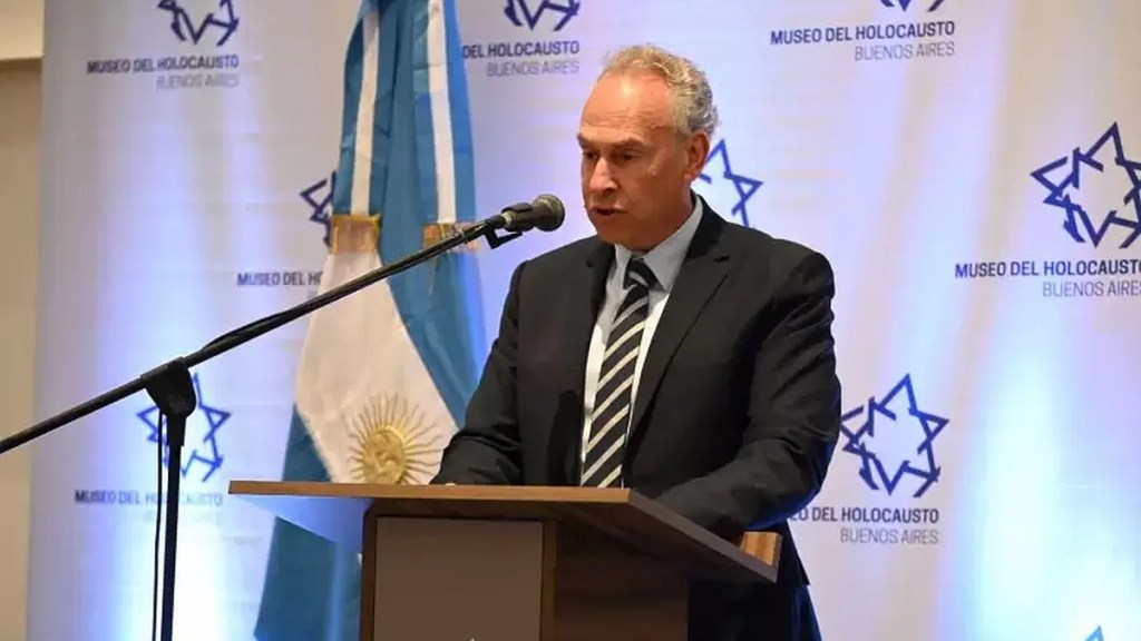 Orador en el Museo del Holocausto de Buenos Aires durante un evento institucional, con una bandera argentina de fondo.