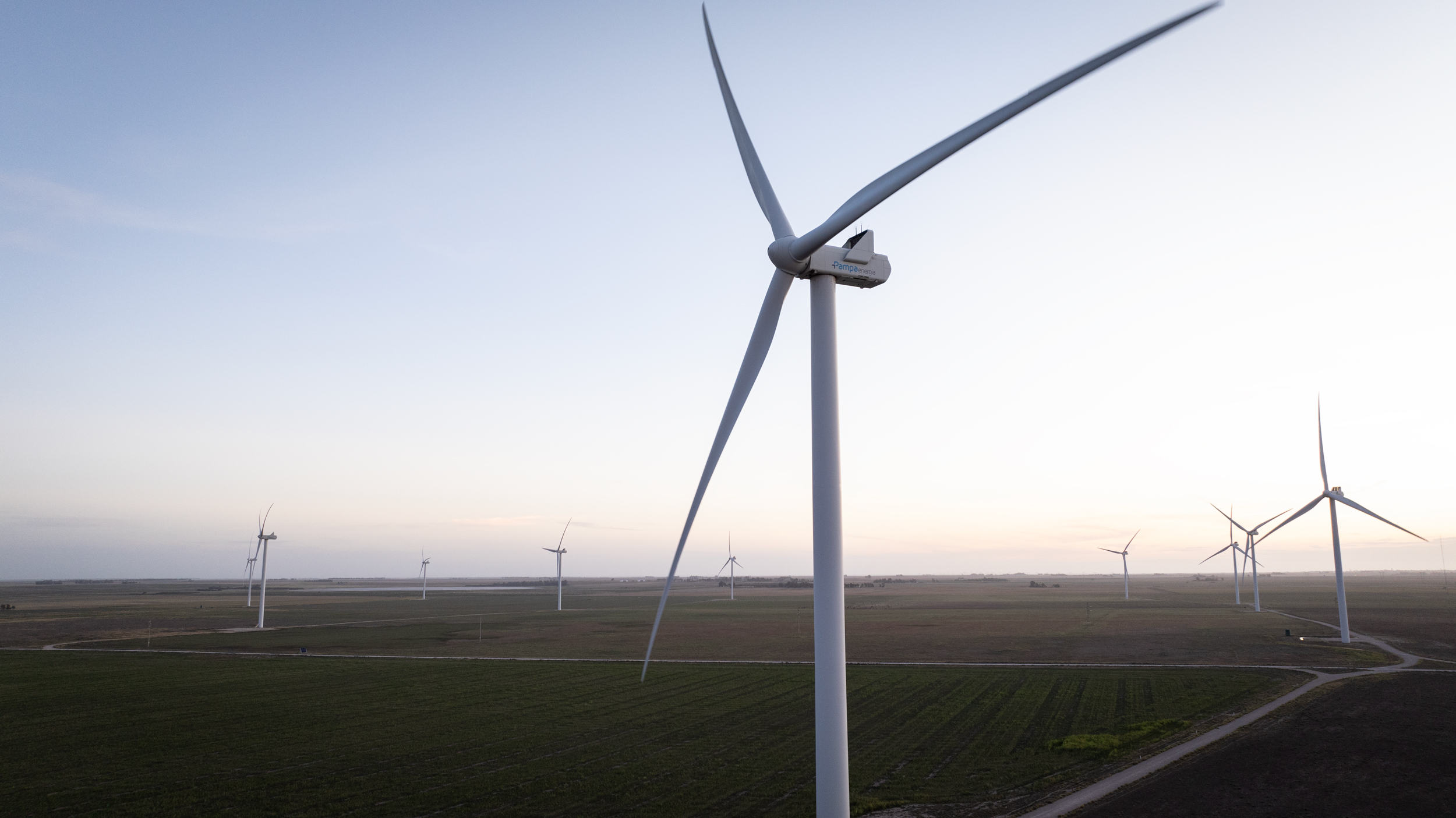 Parque Eólico Pampa Energía VI con aerogeneradores en operación sobre un extenso campo al atardecer, destacando el compromiso con las energías renovables.